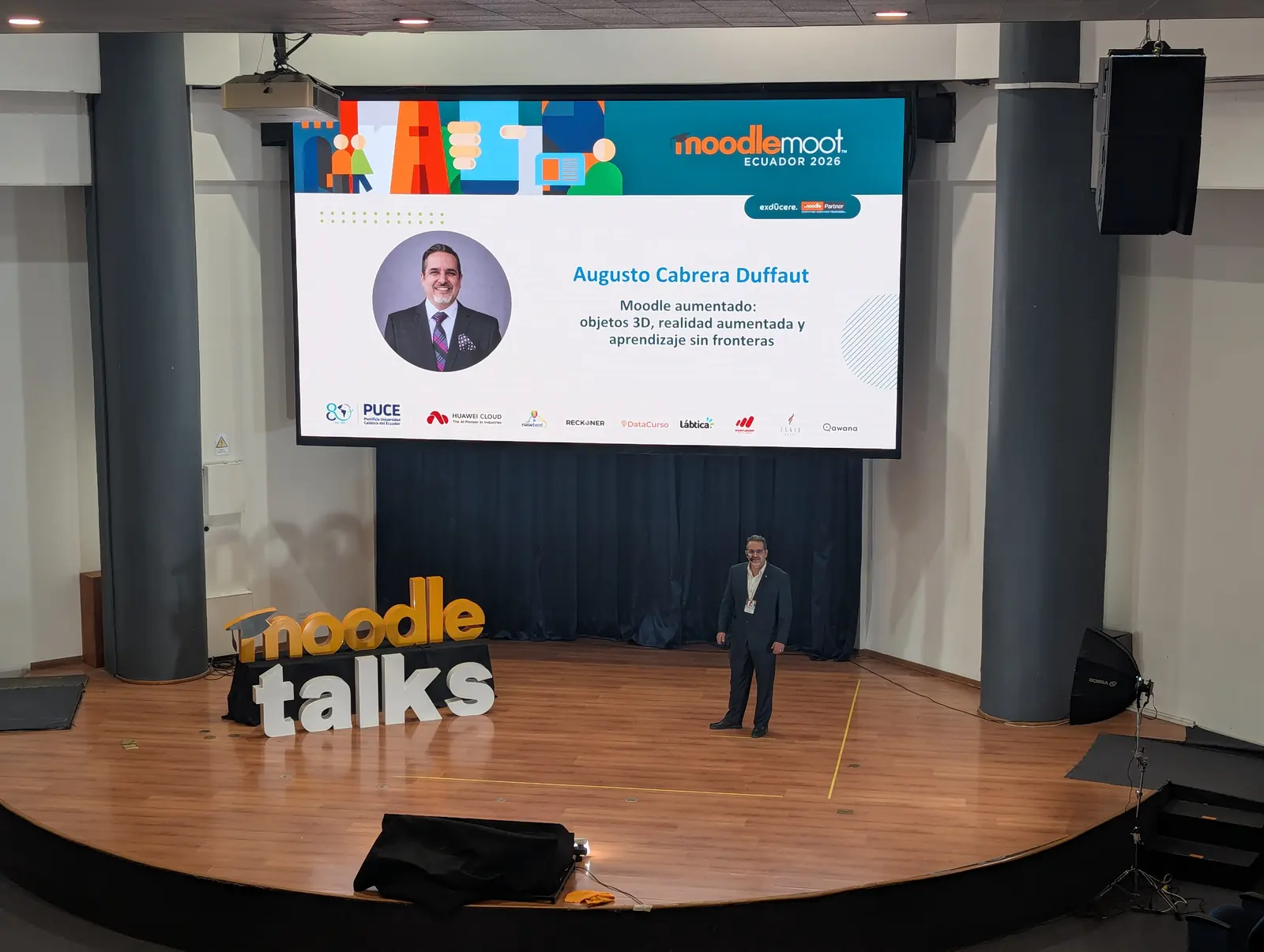 Speaker en el escenario de Moodle Talks durante MoodleMoot Ecuador 2026, con su presentación en la pantalla