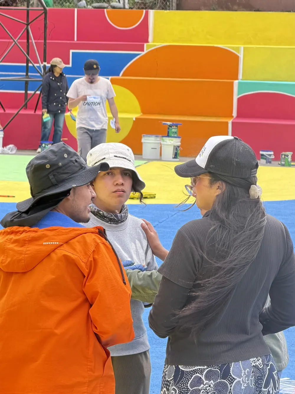 Jóvenes conversando sobre la cancha recién pintada, frente a las gradas intervenidas con colores